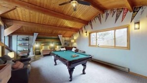 Une table de billard dans une pièce dotée de plafonds en bois et d’une grande fenêtre.