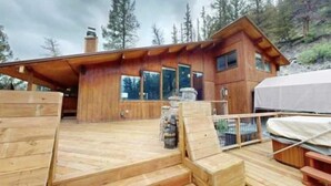 Une cabane en bois dotée d’une terrasse, de grandes fenêtres et d’une cheminée en pierre.