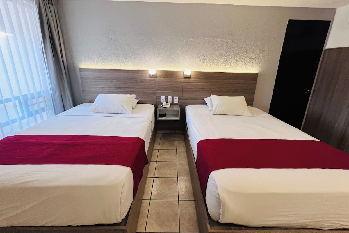 Una habitación de hotel con dos camas, una mesita de noche con teléfono e iluminación de pared.