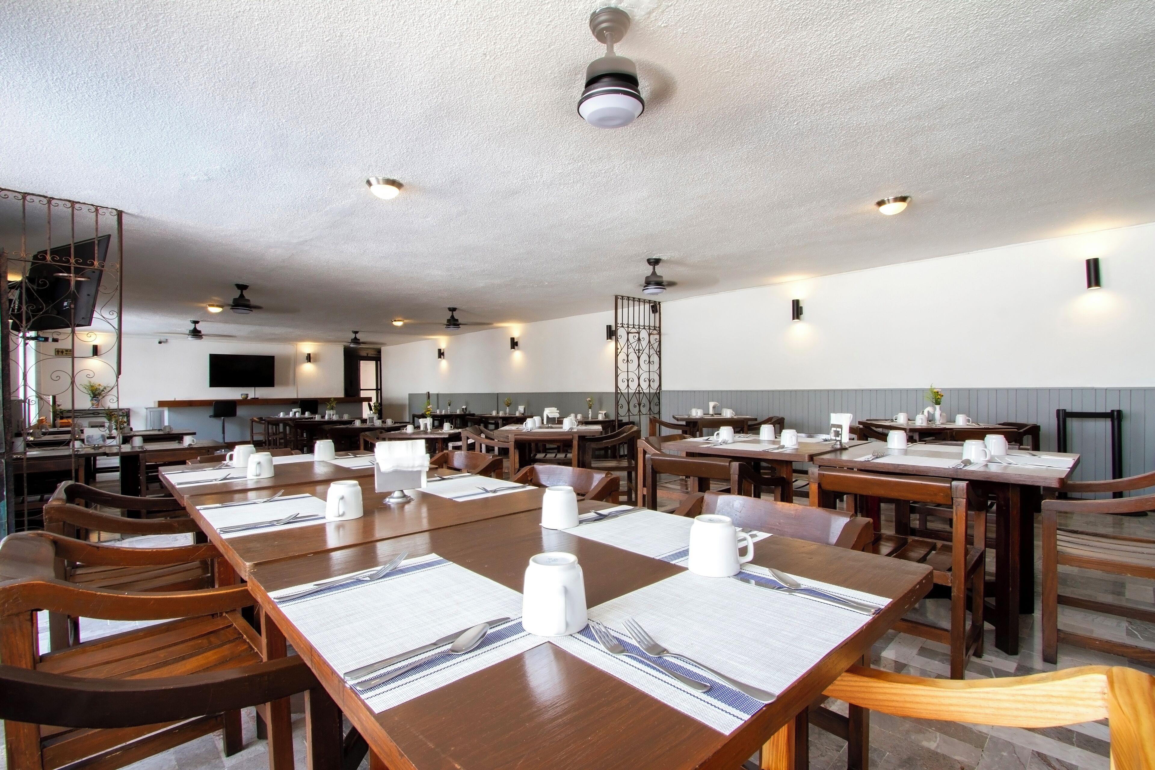 A spacious dining area with multiple wooden tables and chairs, equipped with white placemats and cutlery.