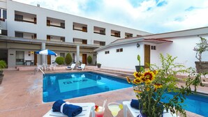 A poolside area with lounge chairs, a pool, and a table with drinks and a vase of flowers. - Hotel Bedd Express Querétaro (Querétaro)