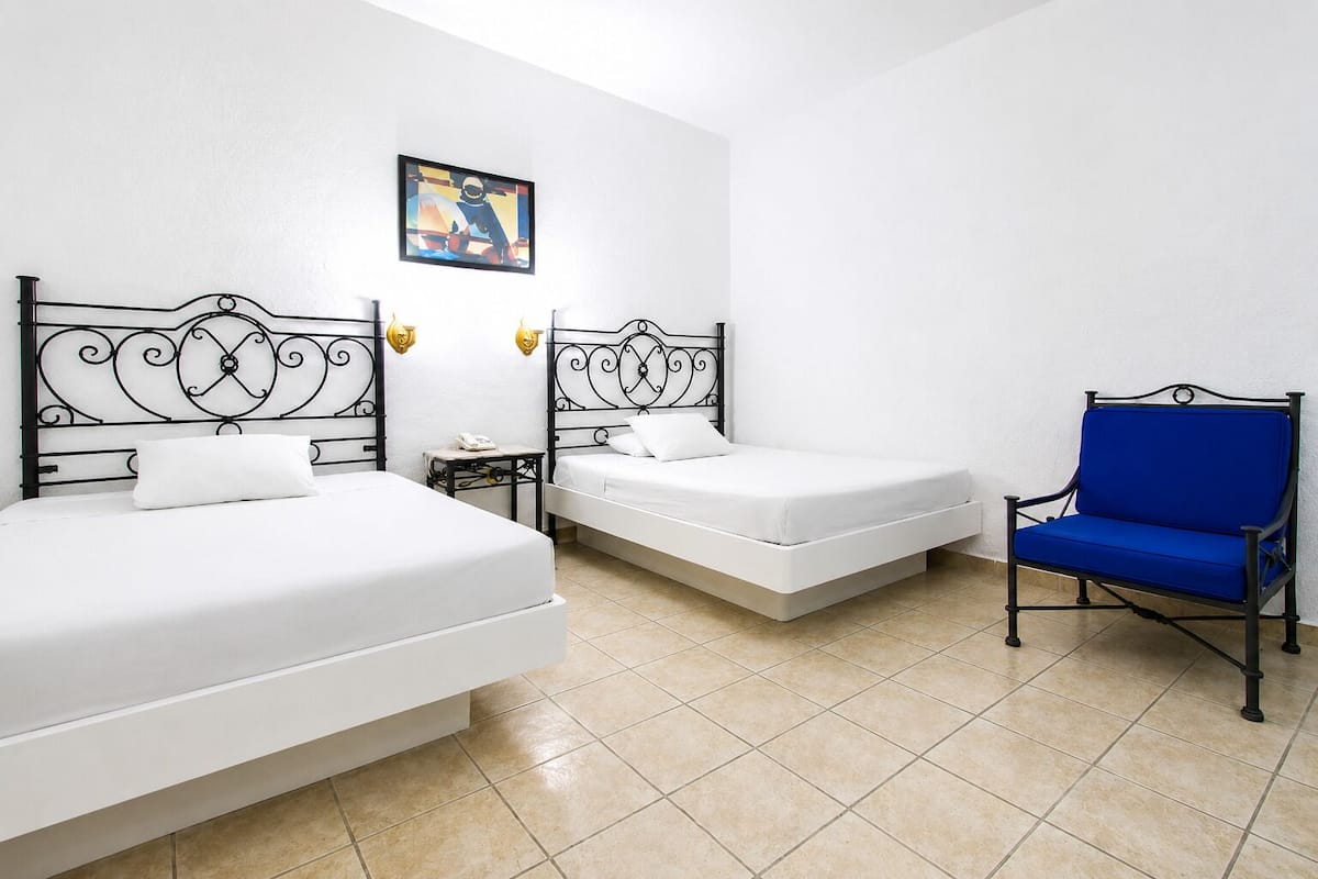 Habitación de hotel con dos camas, una silla azul y una mesita con un teléfono.