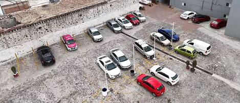 Vista aérea de un estacionamiento con varios coches aparcados en filas, rodeado de edificios con tejados rojos y una pared de hormigón.