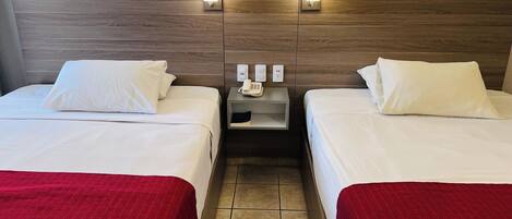 Habitación de hotel con dos camas, una mesita de noche con teléfono y una lámpara fijada a la pared.