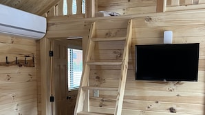 Een houten interieur met een houten ladder, een zwarte prullenbak en een wandgemonteerde flatscreen televisie.