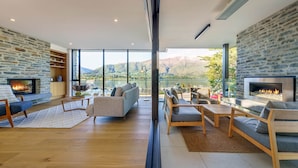 A spacious living room with a stone fireplace, comfortable seating, and a large window offering a lake view. - Marina Terrace Apartments (Wanaka)