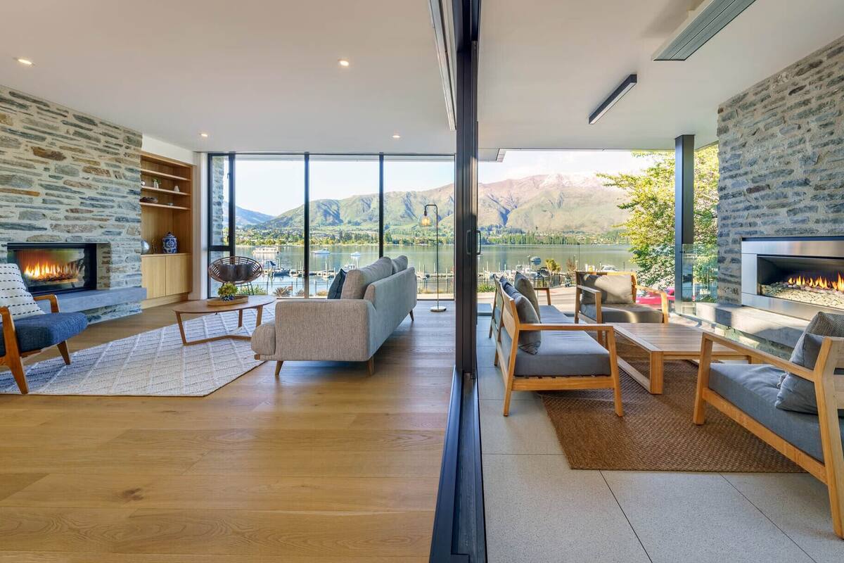 A spacious living room with a stone fireplace, comfortable seating, and a large window offering a lake view.