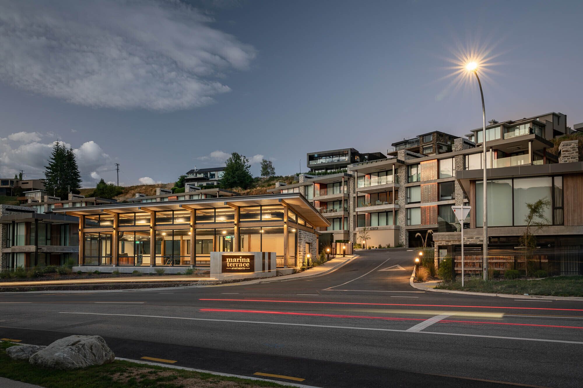 A modern apartment complex with a glass facade, a sign reading "Marina Terrace Apartments," and a well-lit entrance.