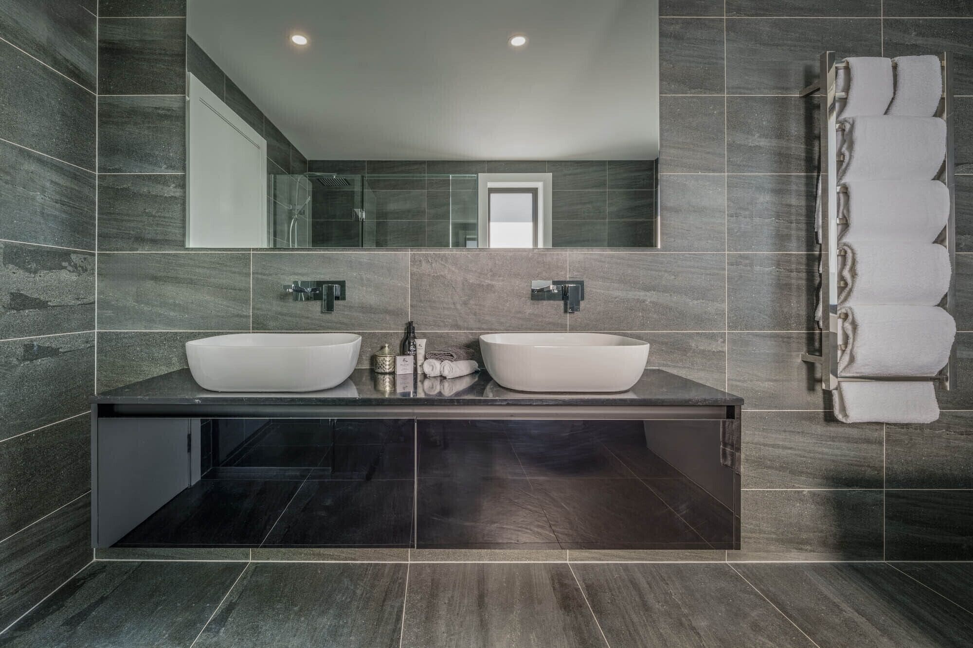 A modern bathroom with two large vessel sinks, a large mirror, and a towel rack.