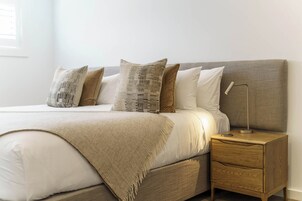 Un lit bien fait, avec une tête de lit grise, une lampe de chevet et une table de chevet en bois dotée de tiroirs.