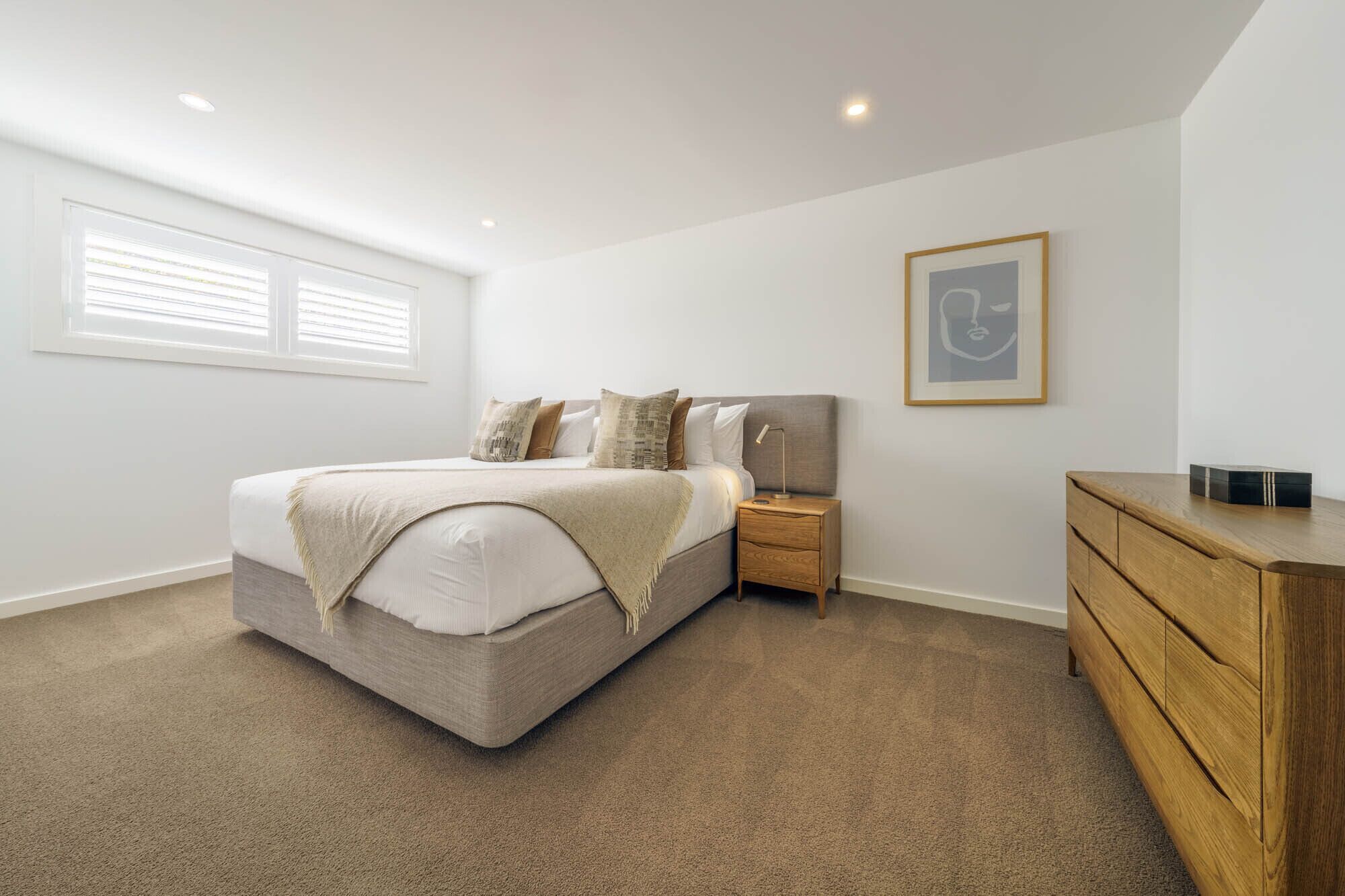 A bedroom with a bed, nightstand, dresser, and a framed picture on the wall.