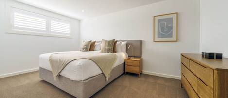 A bedroom with a bed, nightstand, dresser, and a framed picture on the wall.