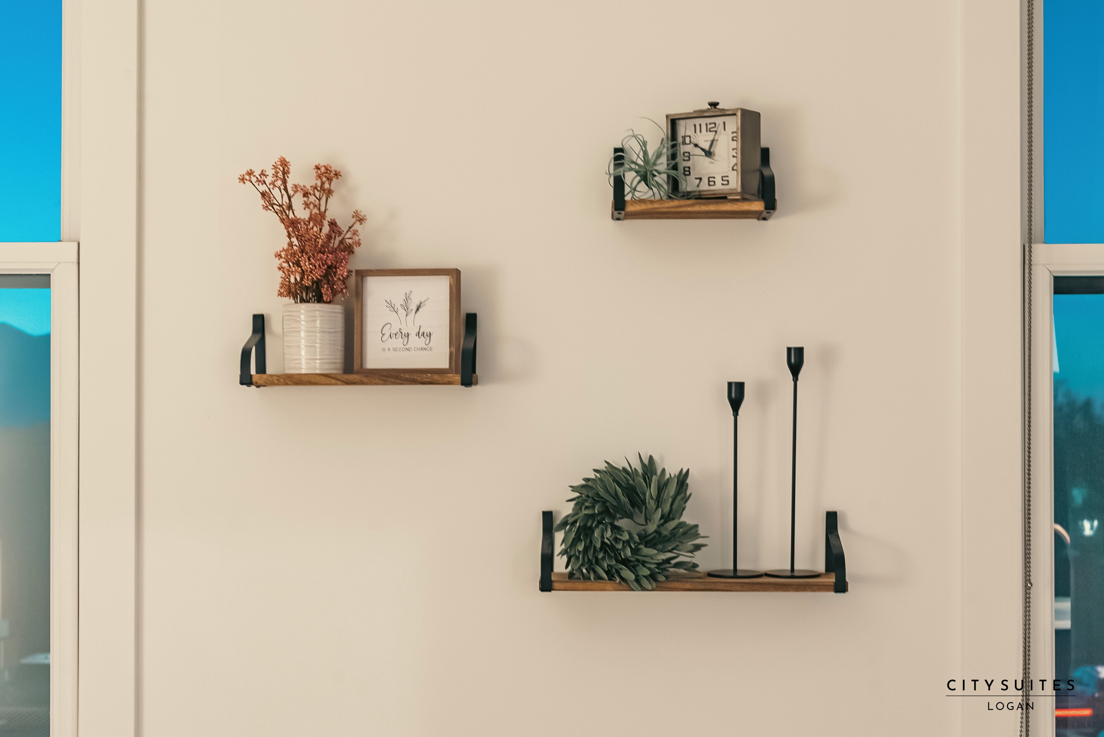 Three wall-mounted shelves with decorative items including a clock, a framed picture, and a vase with dried flowers.