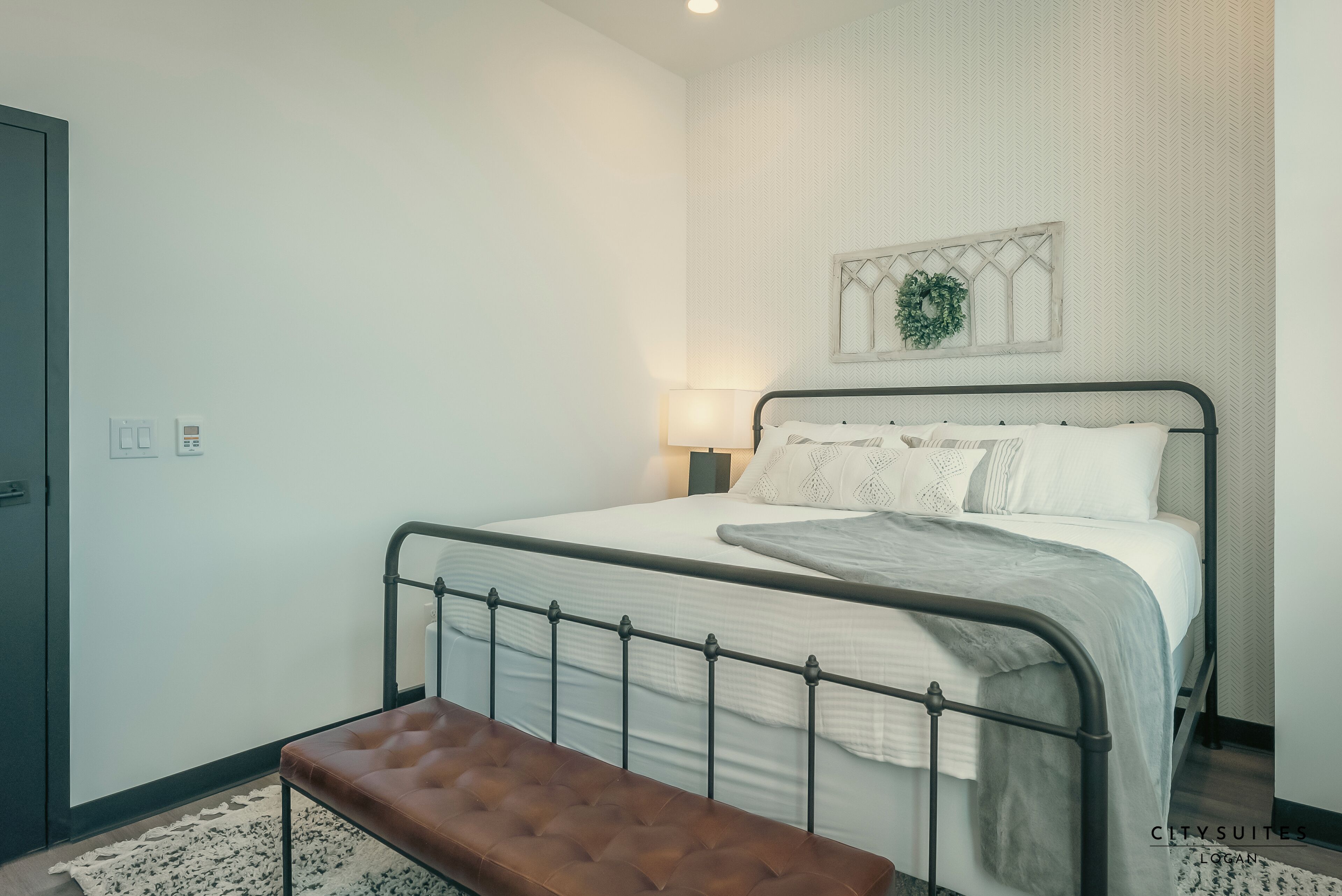 A neatly arranged bedroom with a bed, bench, and a wall-mounted light fixture.