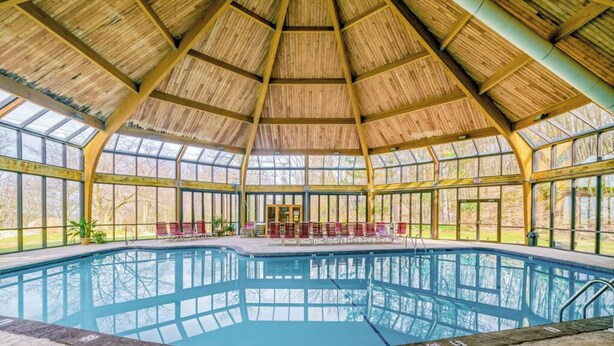 Piscina interna com teto de madeira e grandes janelas.