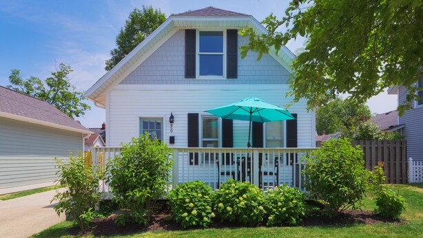 A two-story house with a front porch, a covered patio area with an umbrella, and a well-maintained garden.