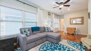 A living room with a grey sectional sofa, a patterned rug, a ceiling fan, and a wooden dresser.