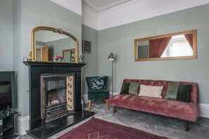 Un salon avec une cheminée, un canapé, un fauteuil et un grand miroir.
