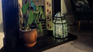 Een haard met daar boven een decoratieve spiegel, een plant in pot en een lantaarn op een vloerkleed.