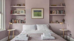 Een slaapkamer met een bed, twee nachtkastjes, een boekenkast en een lijst aan de muur.