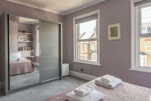 Un dormitorio con cama, armario, ventana y radiador.