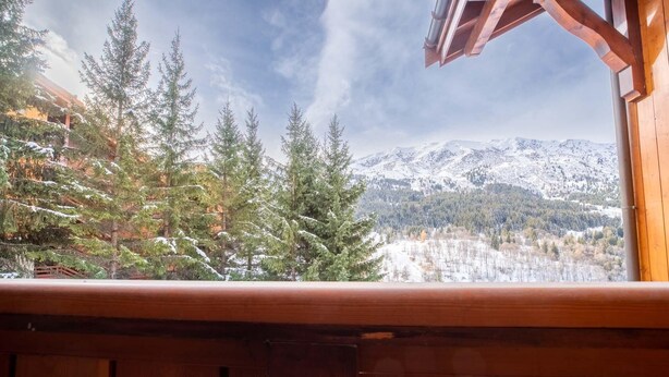 A wooden balcony with a view of snow-covered mountains and evergreen trees. - Krystor 4 in the center of Meribel (Les Allues)