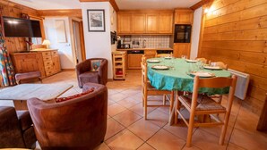 A cozy cabin interior with a dining area, wooden cabinets, a kitchen with appliances, and a television. - Krystor 4 in the center of Meribel (Les Allues)