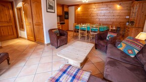 A cozy living room with wooden walls, a dining area with a green tablecloth, and two brown sofas with colorful cushions. - Krystor 4 in the center of Meribel (Les Allues)