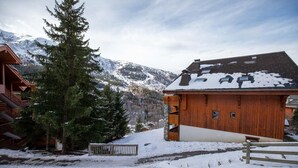 A wooden building with a sloped roof, surrounded by snow-covered ground and a mountain in the background. - Krystor 4 in the center of Meribel (Les Allues)