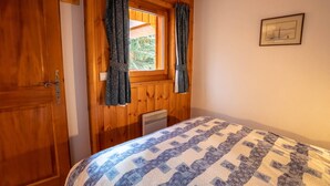 A room with a wooden door, a window with curtains, a bed with a patterned bedspread, and a framed picture on the wall. - Krystor 4 in the center of Meribel (Les Allues)