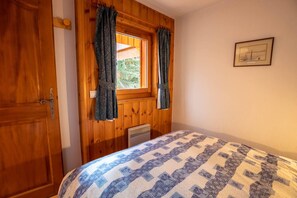 A room with a wooden door, a window with curtains, a bed with a patterned bedspread, and a framed picture on the wall. - Krystor 4 in the center of Meribel (Les Allues)