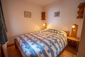 Een slaapkamer met een bed, een houten hoofdbord, twee wandlampen en twee ingelijste foto’s aan de muur.