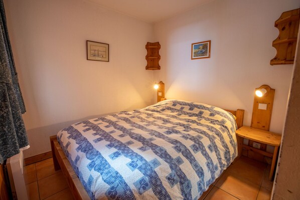 A bedroom with a bed, a wooden headboard, two wall-mounted lights, and two framed pictures on the wall. - Krystor 4 in the center of Meribel (Les Allues)