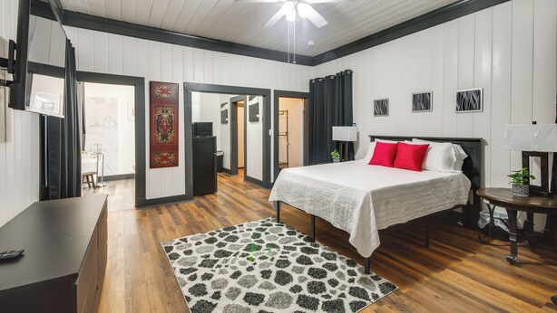 Un dormitorio con cama, escritorio, silla, ventilador de techo y una puerta que da a otra habitación.