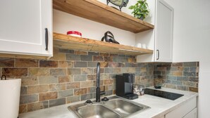 Una cocina con un lavamanos doble, una cafetera y una estantería con una planta y un recipiente rojo.
