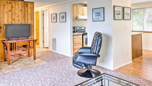 Un salon avec un téléviseur, un fauteuil en cuir, une cheminée et une cuisine à l’arrière-plan.