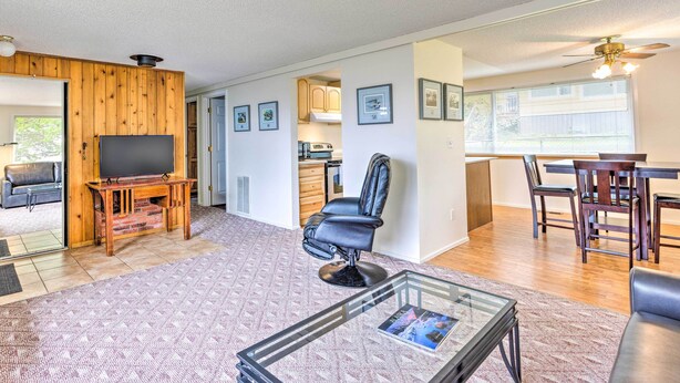 Un vaste espace de vie agrémenté d’un mur en bois, d’un téléviseur à écran plat, d’un fauteuil en cuir, d’une table basse en verre et d’un coin repas avec des chaises et une table en bois.
