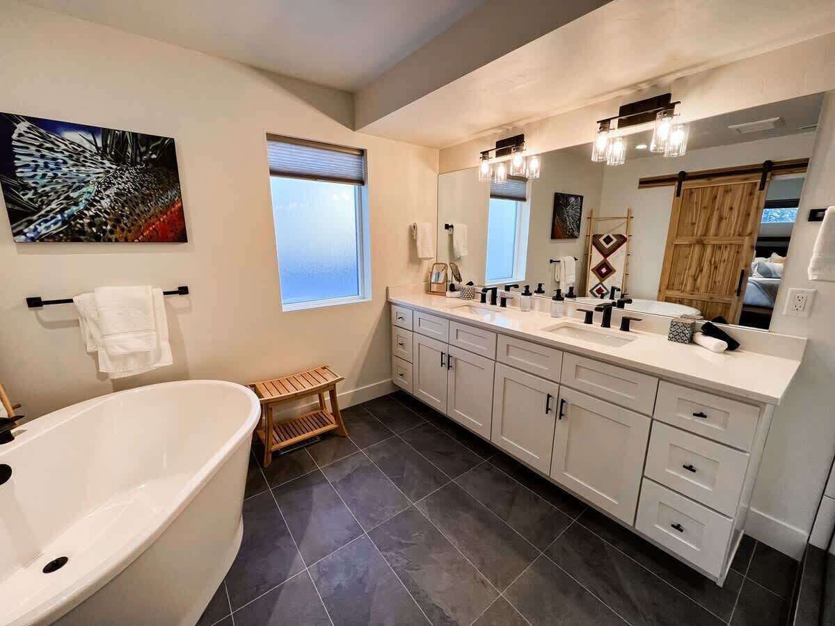 A modern bathroom with a freestanding bathtub, a large vanity with a mirror, and a window providing natural light.