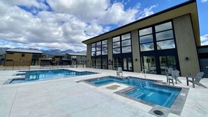 A modern building with large windows, a pool area with multiple pools, and outdoor seating. - Pet Friendly | Pool & Hot Tub | Close to Downtown (Whitefish)