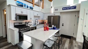 A modern kitchen with white cabinets, a large island, stainless steel appliances, and a wooden ceiling. - Pet Friendly | Pool & Hot Tub | Close to Downtown (Whitefish)