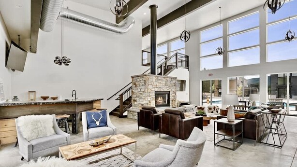 A spacious living area with a stone fireplace, multiple seating arrangements, and large windows offering views. - Pet Friendly | Pool & Hot Tub | Close to Downtown (Whitefish)