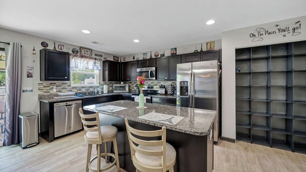 A modern kitchen with dark cabinetry, a stainless steel refrigerator, and a central island with bar stools. - Home away from Home (Lexington)