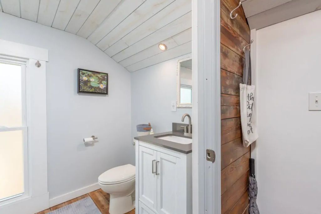 Een badkamer met een wit toilet, een wastafel met een spiegel erboven en een houten wand.