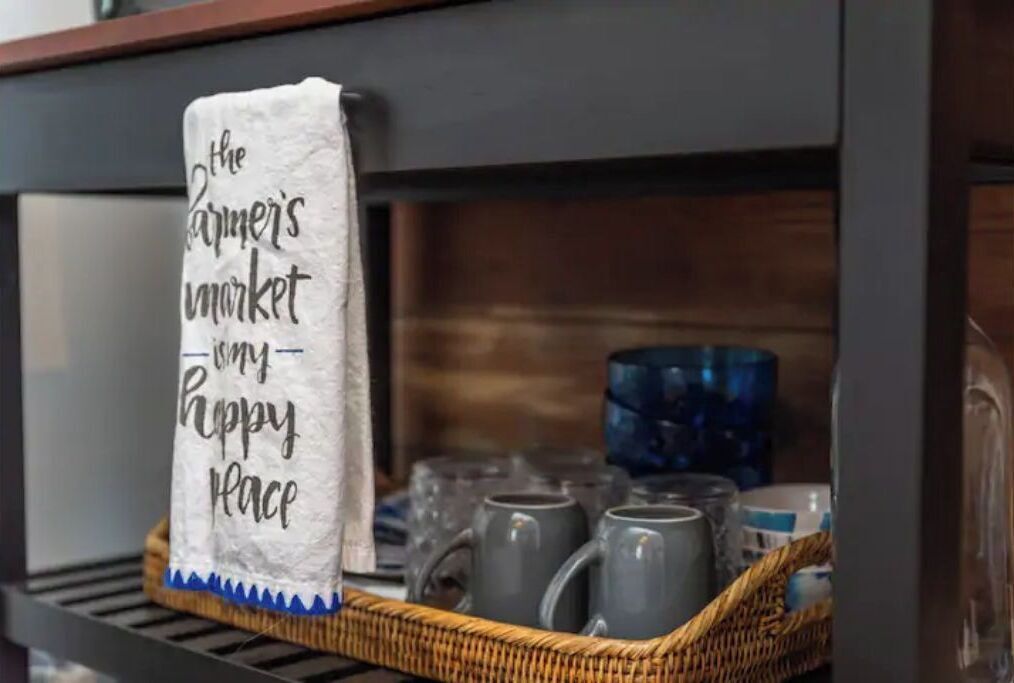 A kitchen shelf with a wicker basket containing mugs and a white towel with text.