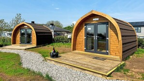 Duas cabanas em formato de cápsula de madeira, com portas de vidro e um pequeno deck de madeira à frente.