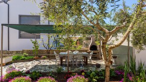 Un patio exterior con suelo de baldosas de piedra, una mesa y sillas, un horno de pizza y una pérgola que da sombra.