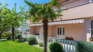 Un edificio de dos plantas con balcón, una palmera y plantas en macetas.