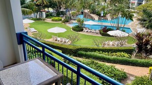 Ein Balkon mit Blick auf einen Poolbereich, einschließlich Liegestühlen und einem gepflegten Rasen.