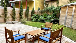 A wooden deck with a table and four chairs, surrounded by a well-maintained garden and a wooden fence. - Charming Southern Cottage (Savannah)
