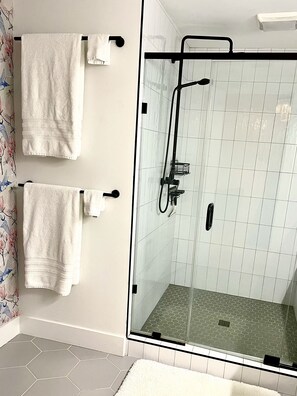 A bathroom with two white towels hanging on black hooks, a glass-enclosed shower with a black hose, and a tiled floor with hexagonal patterns. - Charming Southern Cottage (Savannah)